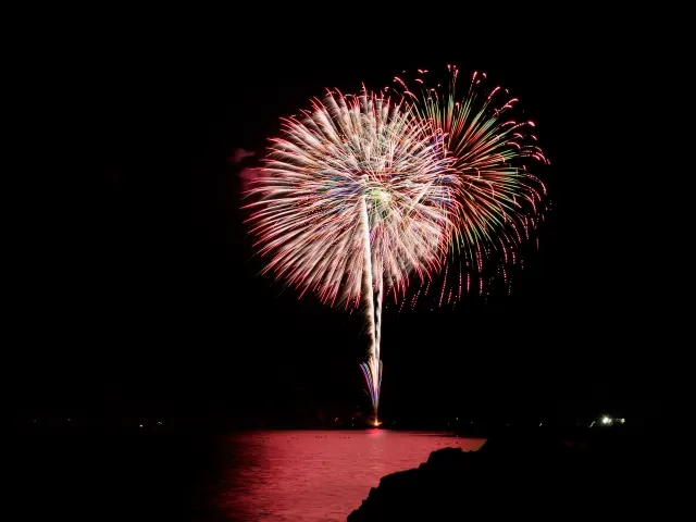 夜の海の上に開き、水面を赤く照らす花火