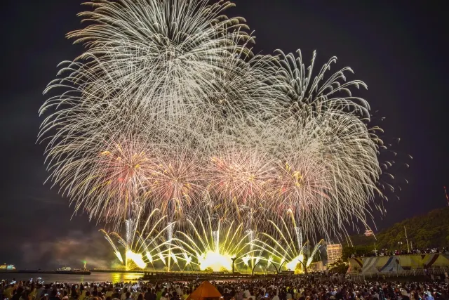 水辺の夜空いっぱいに広がるスターマインと、扇のように開く低い花火