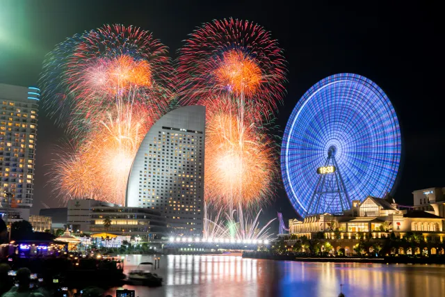 港の夜景と観覧車の向こうに上がる花火